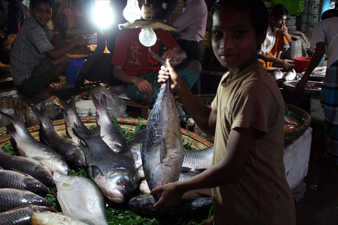 ダッカの市場で魚を持つ少年
